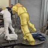 Artist works on a yellow, textured sculpture in a studio, with a white plaster figure nearby. This casting in art is a complex process.