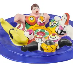 A vibrant ceramic sculpture of Niki de Saint Phalle's Nanas, nestled on a blue plate, bursting with color and playful forms.