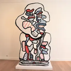 A bold, abstract sculpture in the style of Jean Dubuffet art, featuring a white form outlined in black, filled with red and blue stripes and shapes.