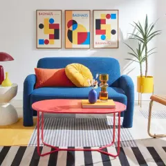 A living room showcasing bauhaus design examples: a blue sofa, geometric art, and colorful furniture.