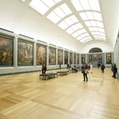 A grand hall showcases what is fine art: large, framed paintings line the walls, with visitors admiring them.