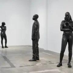 Three striking figures by thomas j price sculpture stand in a minimalist gallery space. One woman poses confidently, another is engrossed in her phone, and a man in a suit stands stoically.