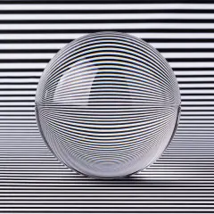 A glass sphere distorts black and white stripes, creating a mesmerizing optical illusion art piece.