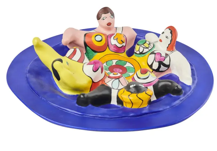 A vibrant ceramic sculpture of Niki de Saint Phalle's Nanas, nestled on a blue plate, bursting with color and playful forms.