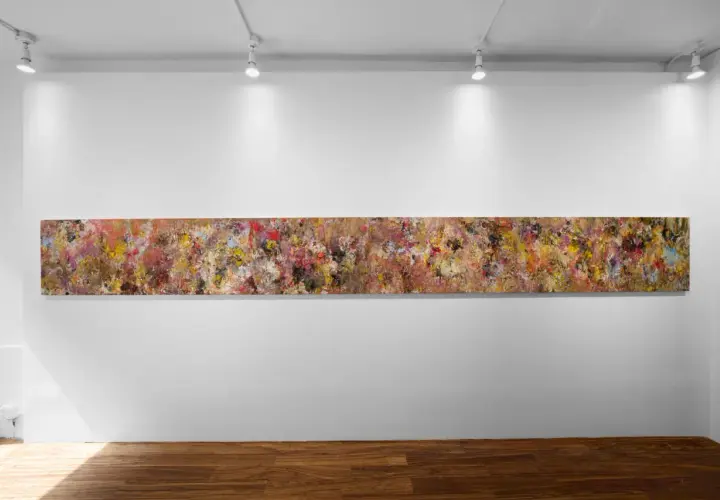 A long, abstract painting by Angela China artist, bursting with vibrant colors and textures, hangs on a white gallery wall.