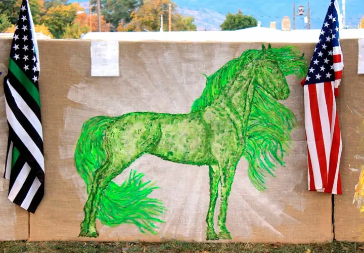 A vibrant green horse painting on burlap, flanked by American flags.