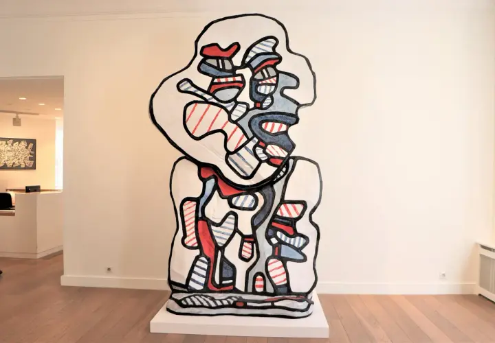 A bold, abstract sculpture in the style of Jean Dubuffet art, featuring a white form outlined in black, filled with red and blue stripes and shapes.