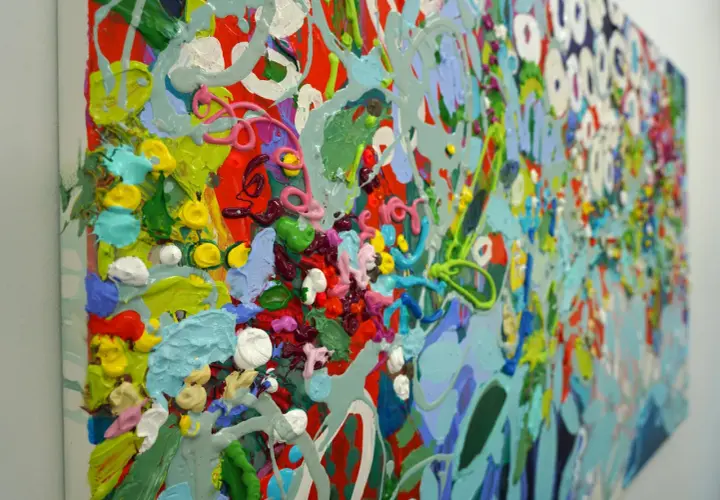 A vibrant, detailed abstract art piece explodes with thick, textured paint in shades of red, green, blue, yellow, and pink, creating a lively, energetic composition.