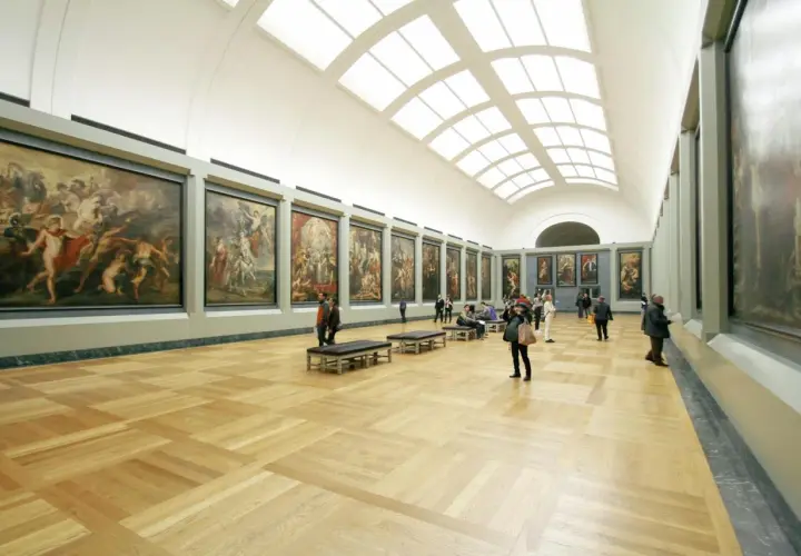 A grand hall showcases what is fine art: large, framed paintings line the walls, with visitors admiring them.