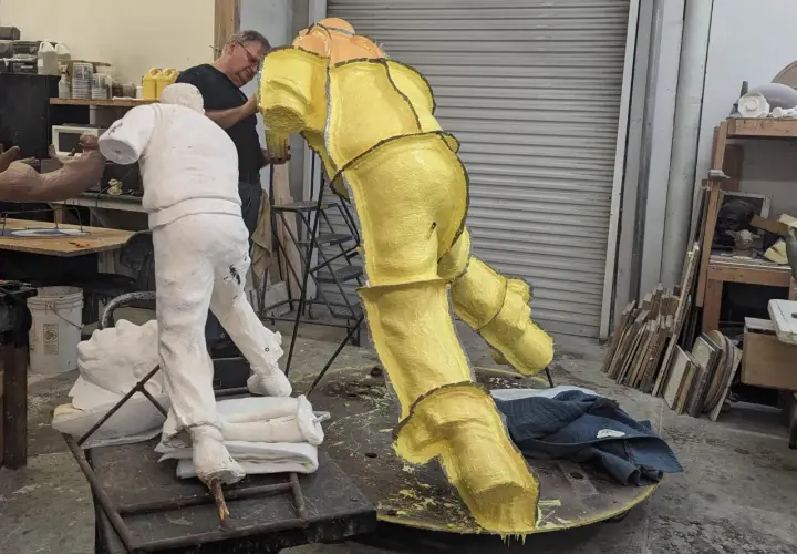 Artist works on a yellow, textured sculpture in a studio, with a white plaster figure nearby. This casting in art is a complex process.