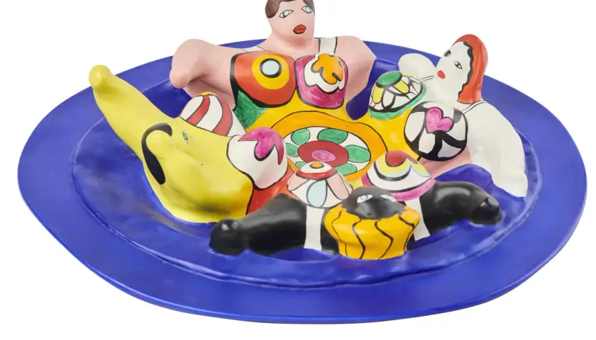 A vibrant ceramic sculpture of Niki de Saint Phalle's Nanas, nestled on a blue plate, bursting with color and playful forms.