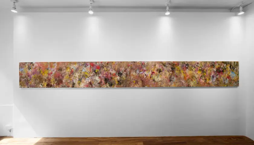 A long, abstract painting by Angela China artist, bursting with vibrant colors and textures, hangs on a white gallery wall.