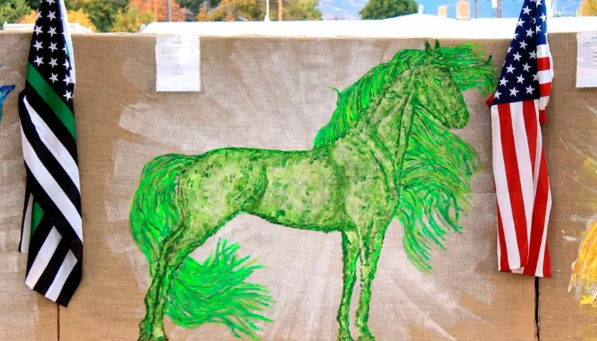 A vibrant green horse painting on burlap, flanked by American flags.