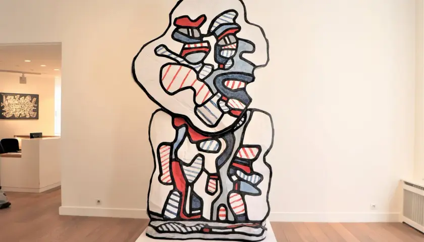 A bold, abstract sculpture in the style of Jean Dubuffet art, featuring a white form outlined in black, filled with red and blue stripes and shapes.