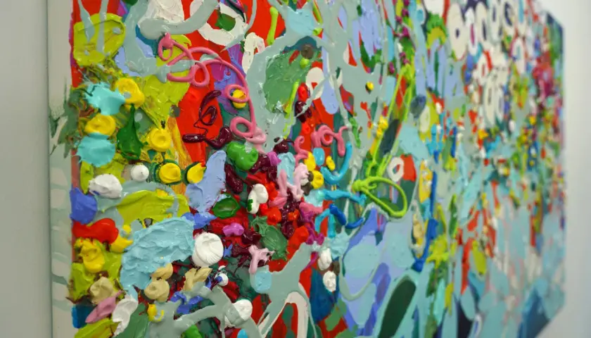 A vibrant, detailed abstract art piece explodes with thick, textured paint in shades of red, green, blue, yellow, and pink, creating a lively, energetic composition.