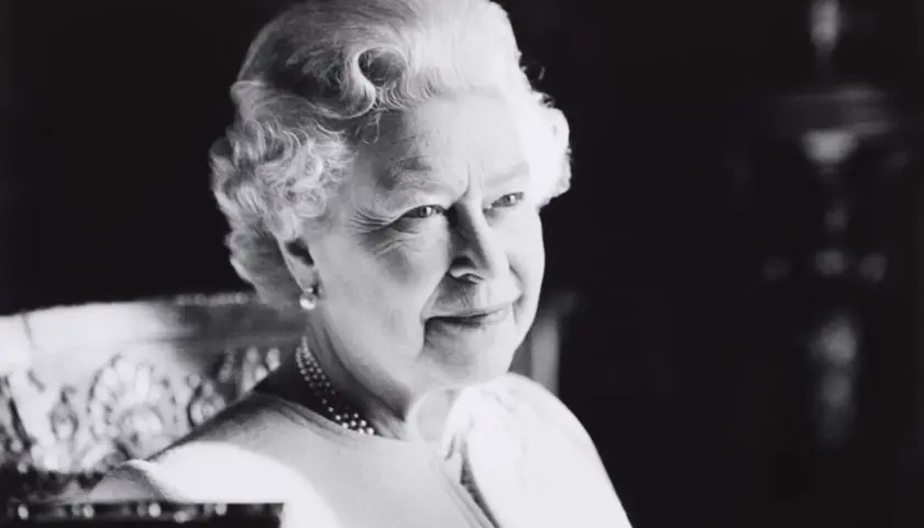 A classic Sutherland portrait of the Queen, her gaze thoughtful, adorned with pearls and a subtle smile.