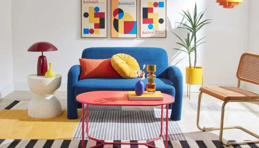A living room showcasing bauhaus design examples: a blue sofa, geometric art, and colorful furniture.
