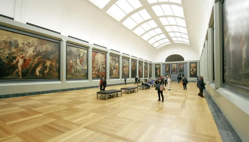 A grand hall showcases what is fine art: large, framed paintings line the walls, with visitors admiring them.