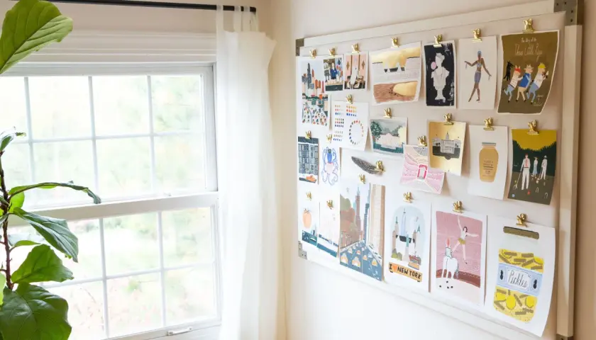 A mood board displays a collection of minimalist contemporary art prints, featuring cityscapes, figures, and whimsical illustrations, all clipped to a white board.