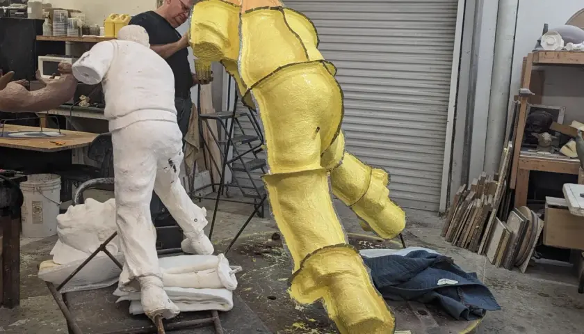 Artist works on a yellow, textured sculpture in a studio, with a white plaster figure nearby. This casting in art is a complex process.