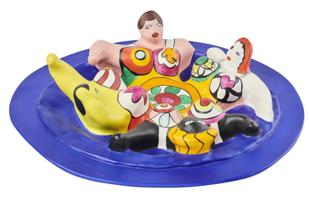 A vibrant ceramic sculpture of Niki de Saint Phalle's Nanas, nestled on a blue plate, bursting with color and playful forms.