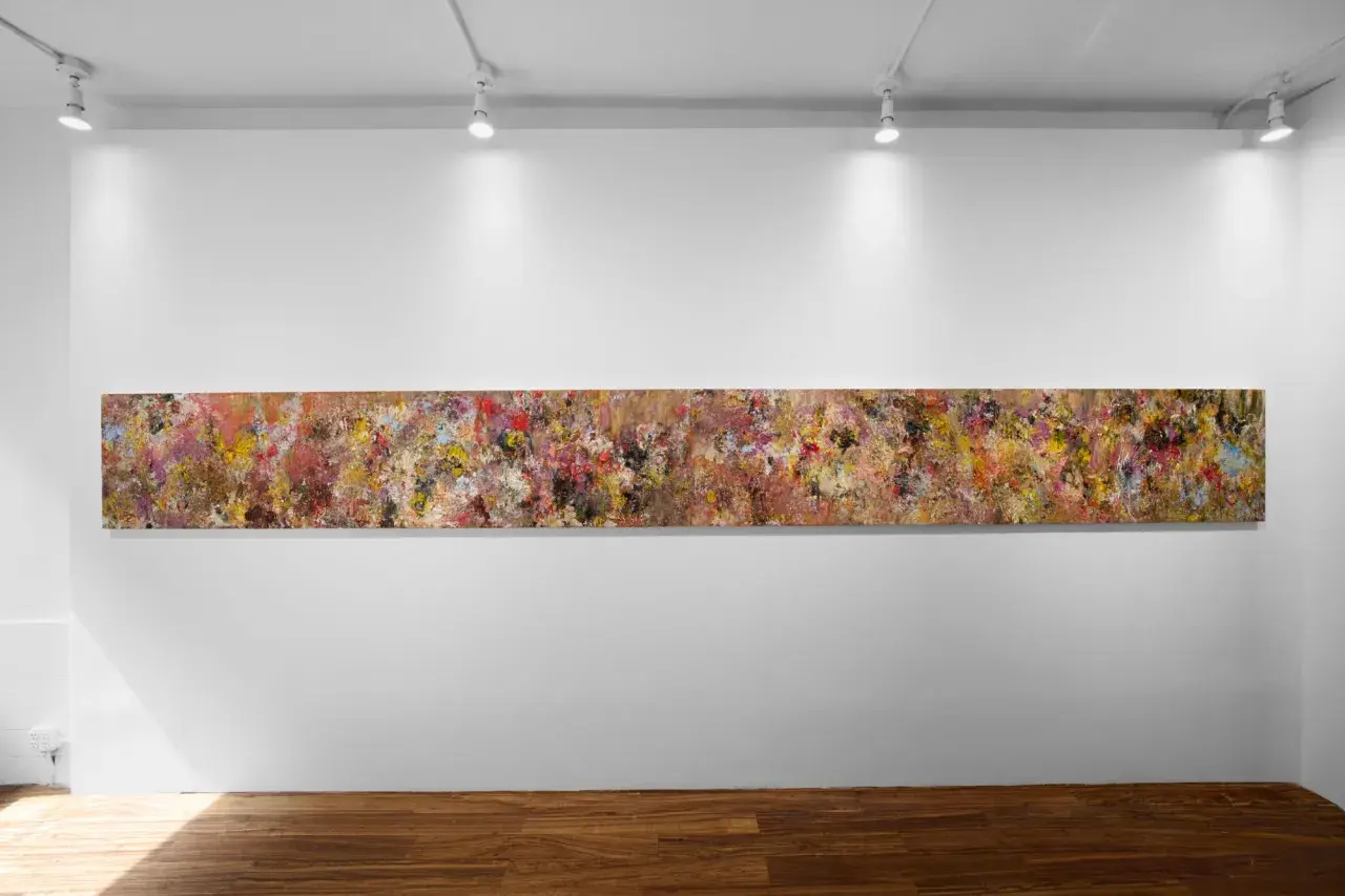 A long, abstract painting by Angela China artist, bursting with vibrant colors and textures, hangs on a white gallery wall.