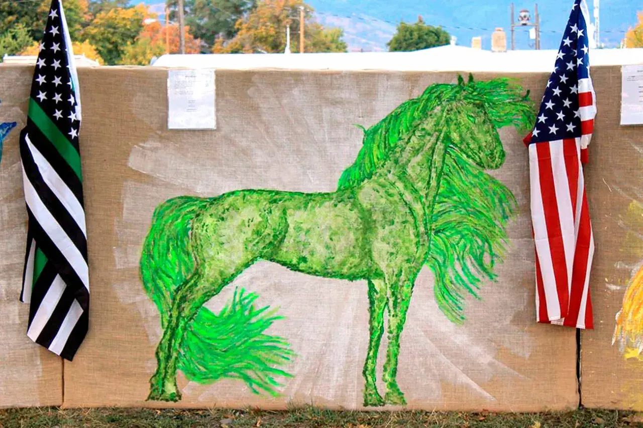 A vibrant green horse painting on burlap, flanked by American flags.