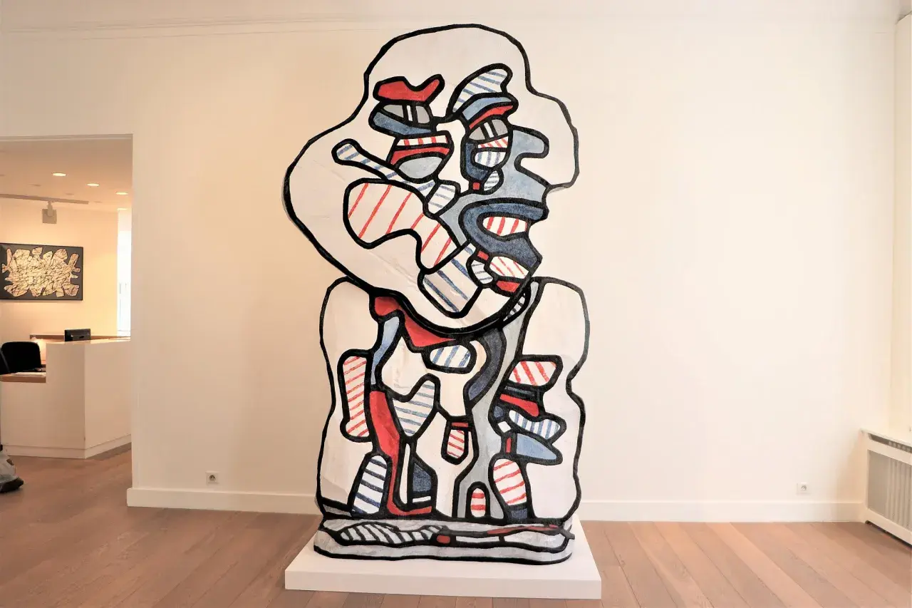 A bold, abstract sculpture in the style of Jean Dubuffet art, featuring a white form outlined in black, filled with red and blue stripes and shapes.