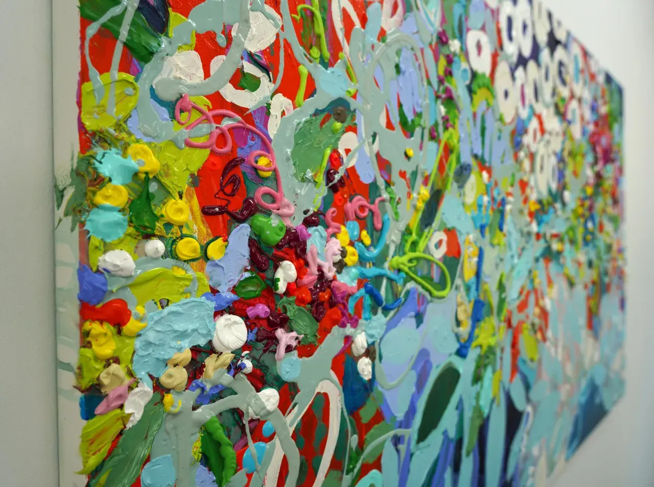 A vibrant, detailed abstract art piece explodes with thick, textured paint in shades of red, green, blue, yellow, and pink, creating a lively, energetic composition.