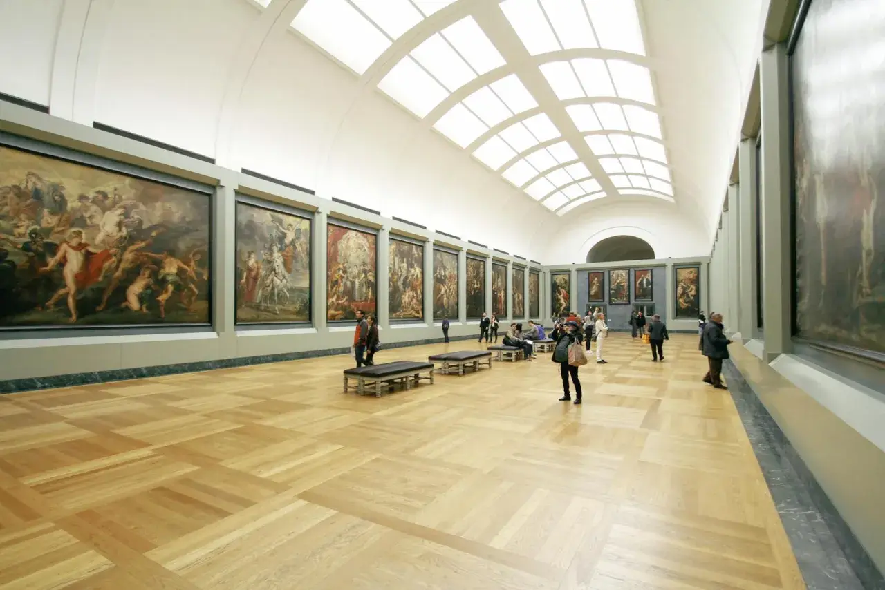 A grand hall showcases what is fine art: large, framed paintings line the walls, with visitors admiring them.