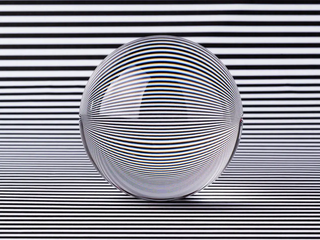 A glass sphere distorts black and white stripes, creating a mesmerizing optical illusion art piece.