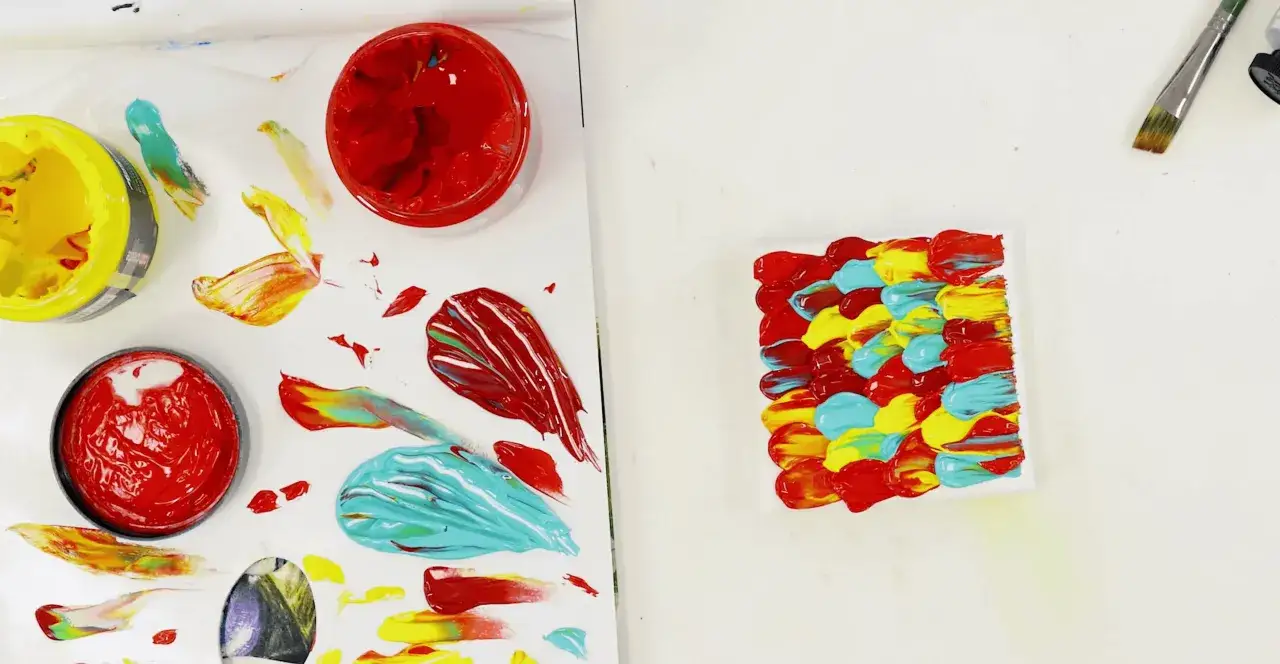 Exploring visual literacy in art: vibrant paint strokes of red, yellow, and teal are applied to a canvas, with open paint pots and swatches nearby.