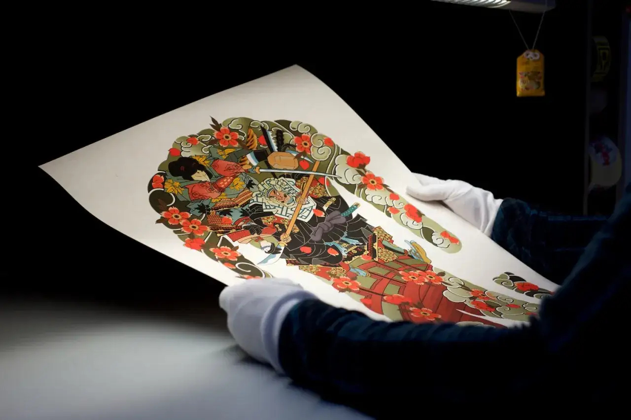 A giclee print showcases a vibrant Japanese warrior surrounded by cherry blossoms. The detailed artwork, a testament to the giclee meaning of high-quality reproduction, is held by gloved hands.