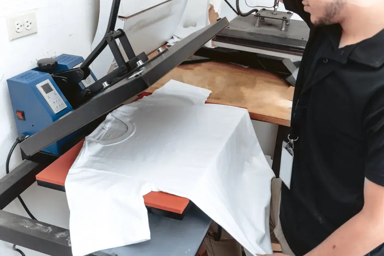 A person prepares a white t-shirt on a heat press, demonstrating how to screenprint custom designs onto apparel.