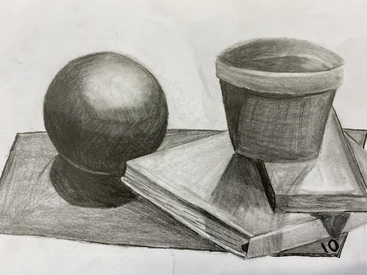 A charcoal still life showcases a sphere, a pot, and books, with masterful use of tone in art to create depth and form.