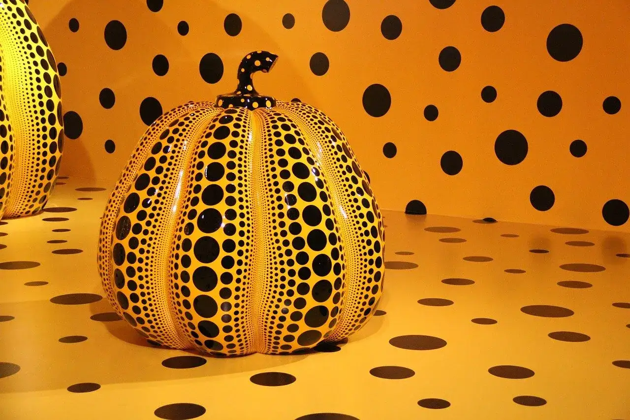 A spotted pumpkin sculpture, a signature of the spotted pumpkin artist, sits in a room adorned with black polka dots on an orange background.