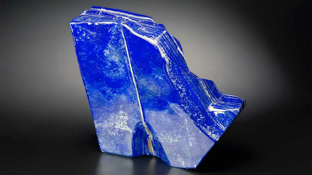 A striking, angular piece of blue lapis lazuli with white inclusions and golden veins, set against a dark background.