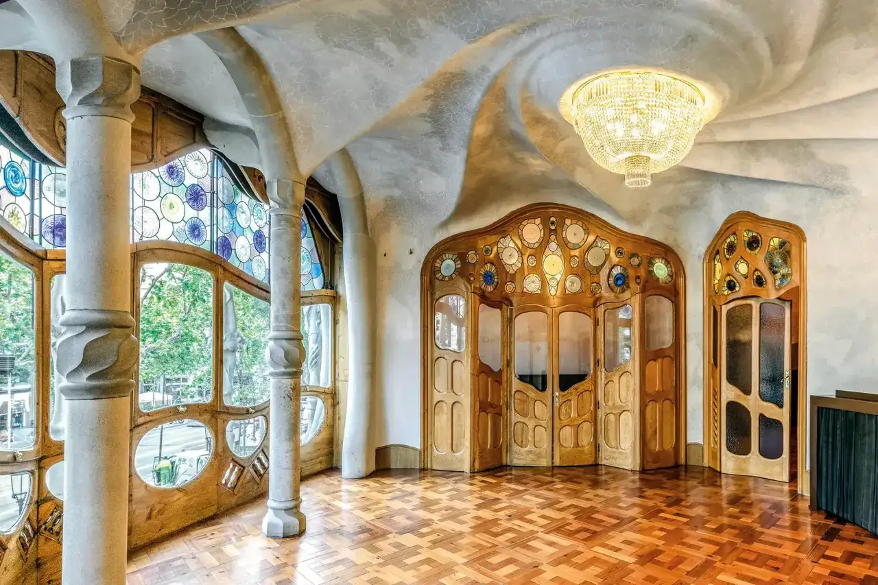 An interior with curved ceilings and columns, stained glass windows, and wooden doors, all in a stunning art nouveau style.