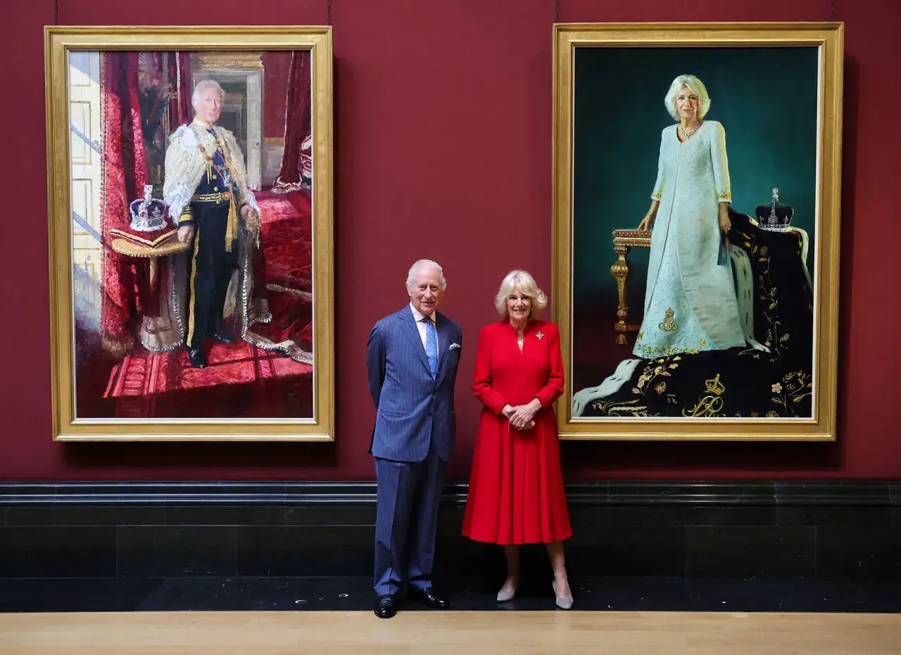 King Charles III and Queen Camilla stand between their portraits. The king's portrait, showing him in regalia, illustrates what are some ways the king's portrait was used: for official display and to project royal authority.